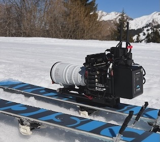 Three people on a beach near an old blue vehicle at sunset
